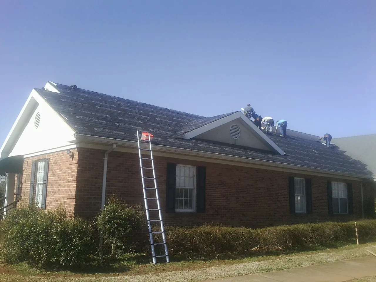 Crew tearing shingles off a brick ranch roof with a ladder set — Emergency Roof Repair work by our crew in Eaton Park
