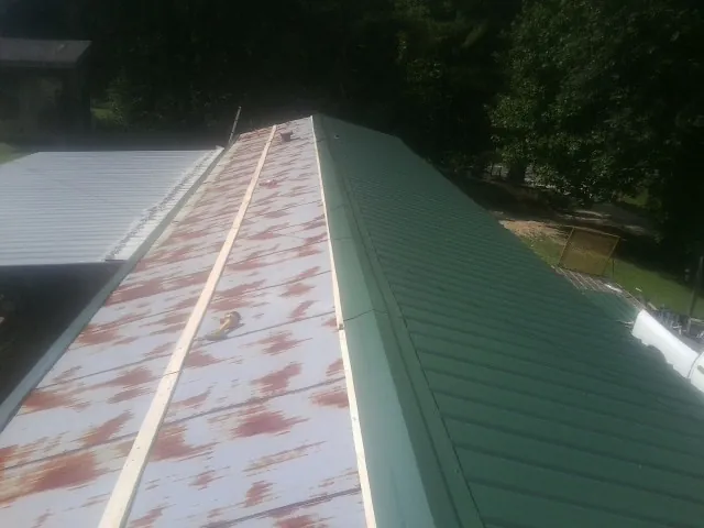Old rusted panels beside newly installed green metal roofing — Wind Damage Roof Repair by Roofing Brothers in Eaton Park