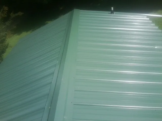 New green metal panels meeting at the ridge of a roof — Flat Roof Repair work by our crew in Eaton Park