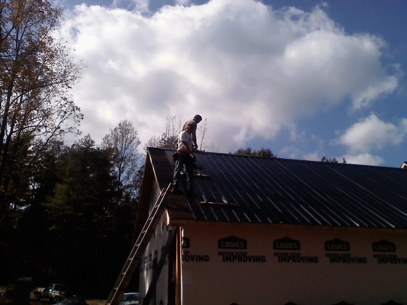 Roofer fastening dark metal panels high against a cloudy sky, from a Roof Inspection job in Eaton Park