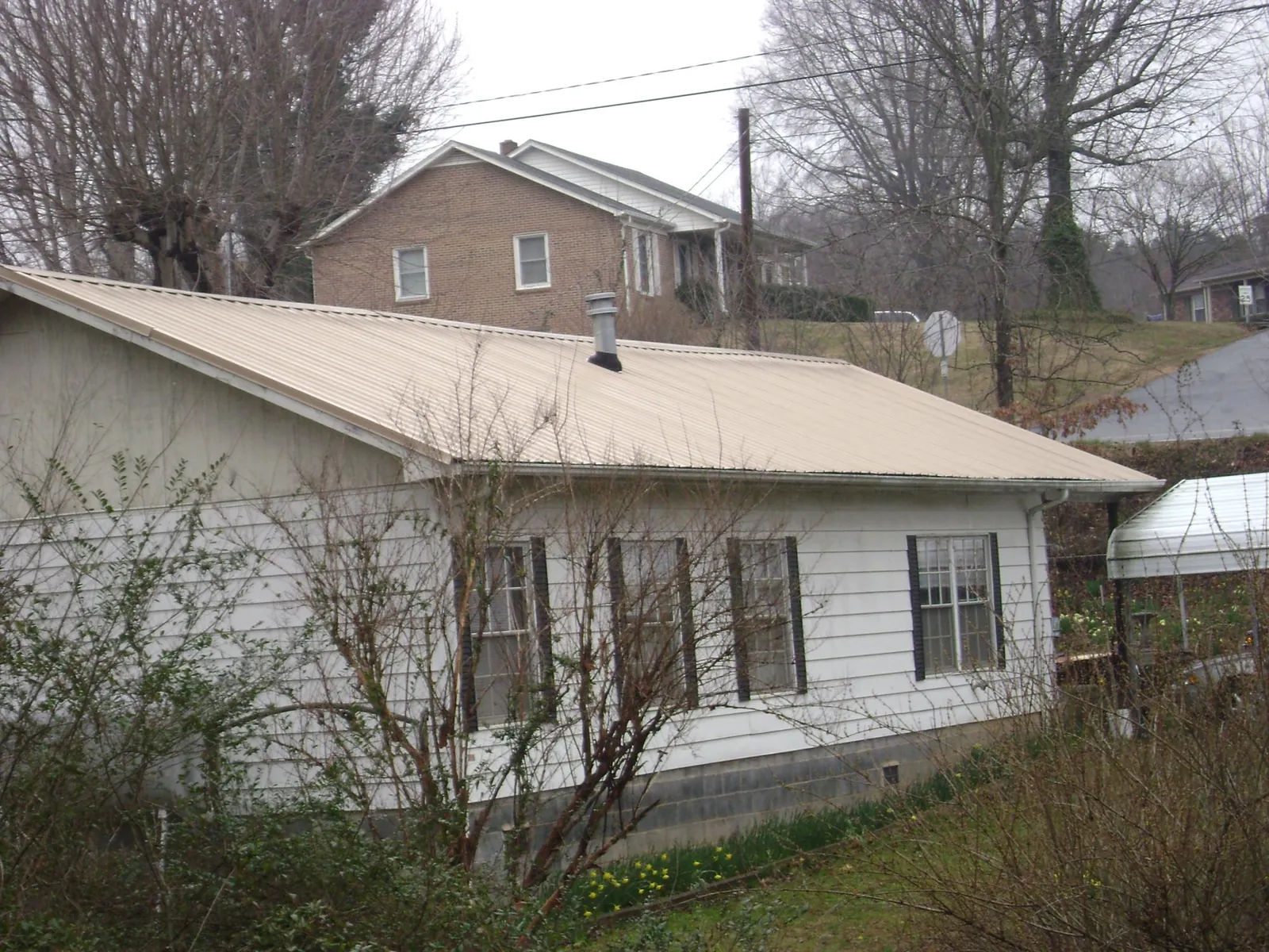 Tan metal roof on a white sided house set into a hillside — Commercial Roofing by Roofing Brothers in Eaton Park