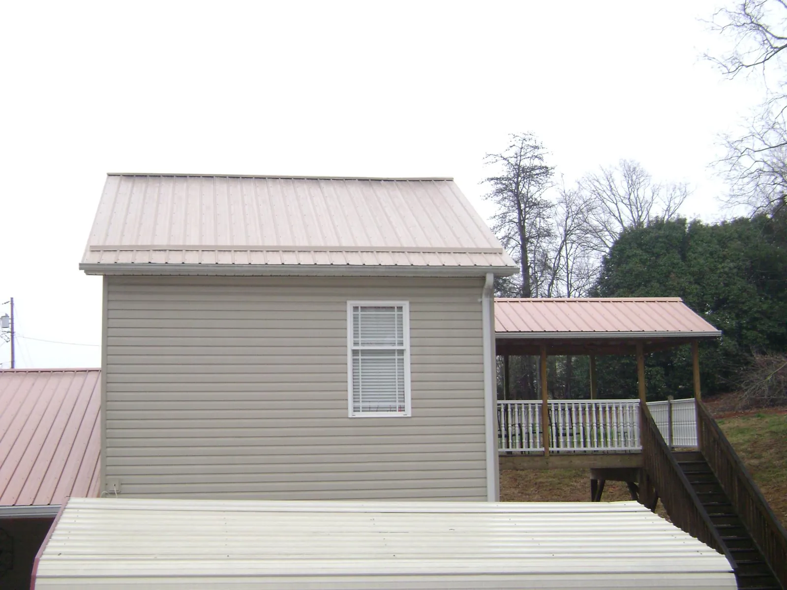 Tan metal roofs on a two story addition and attached porch, from a Roof Replacement job in Eaton Park